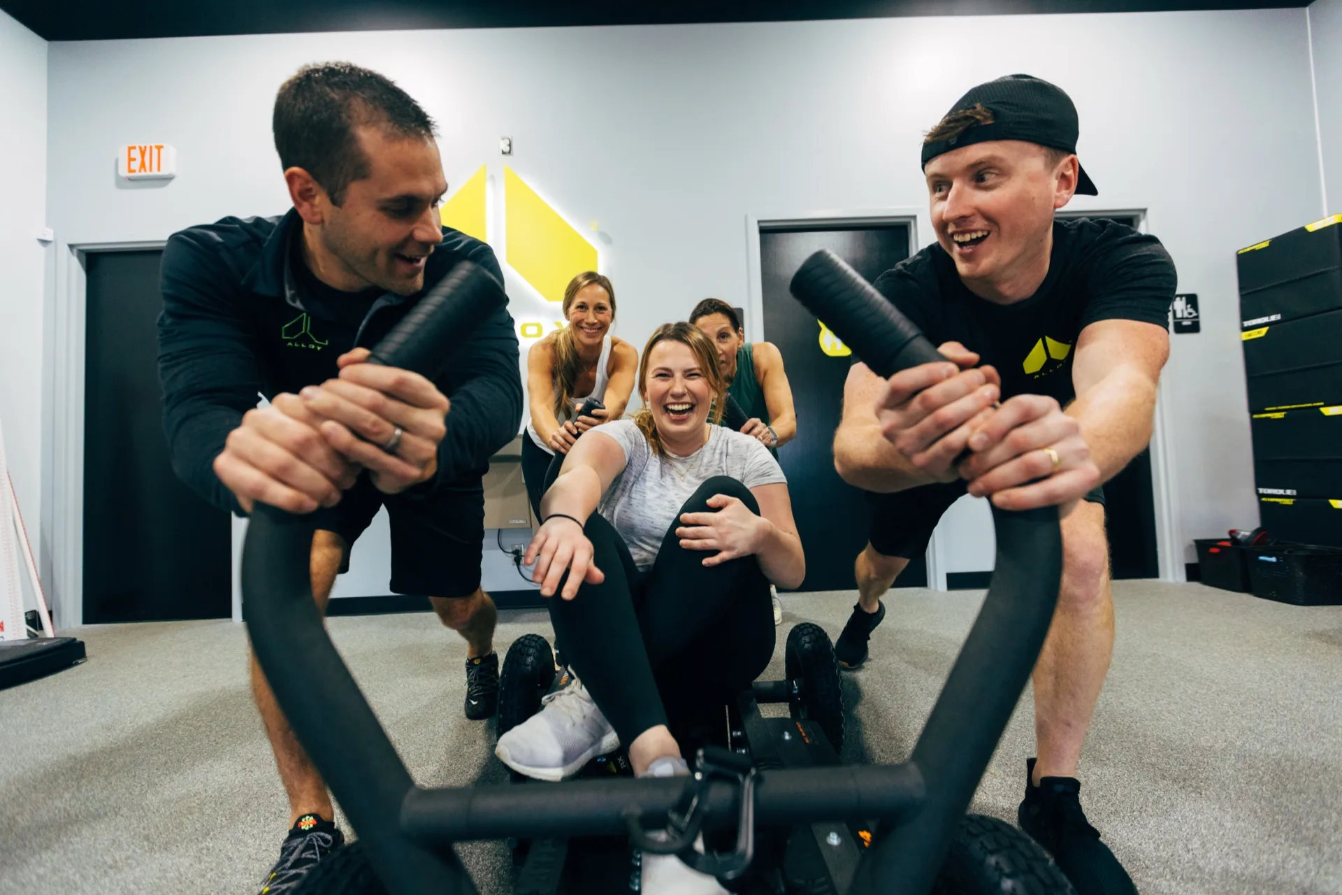 Five laughing members gather around a tank sled after a small group session at Alloy Personal Training in Acworth, GA